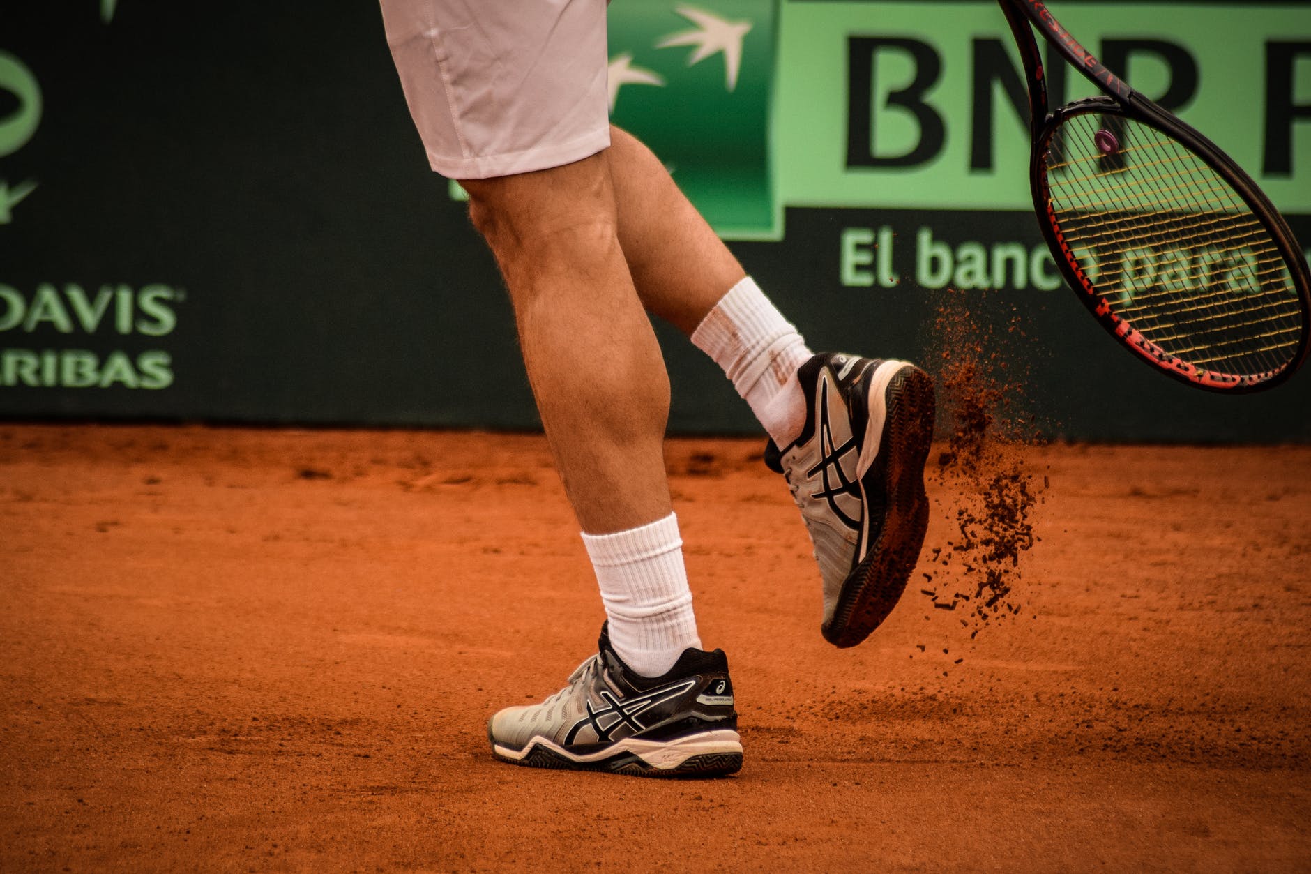 man wearing black and white asics athletic shoes holding racket